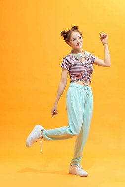 Sarı arka planda zıplayan mutlu Asyalı kız öğrenci