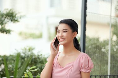 Dışarıda cep telefonuyla konuşan mutlu genç bir kadın.