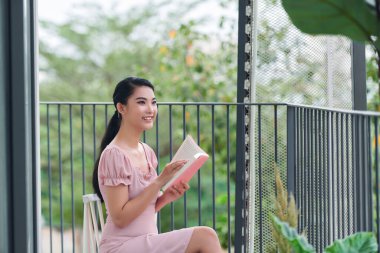 Güzel genç bir kadın balkonda kitap okuyor.