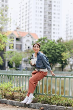 Mutlu, genç, güzel bir kadın elinde kahve fincanı tutarken ve sokakta otururken gülümserken.