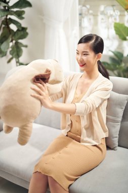 Sarılmak için en iyi arkadaş. Güzel, genç Asyalı bir kadın koltuğunda otururken oyuncak ayısına gülümseyerek sarılıyor.