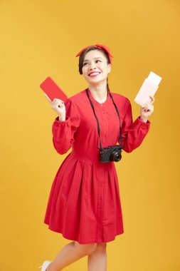 Sarı duvar arkasında izole edilmiş poz veren heyecanlı genç kadın turist görüntüsü. Elinde biletlerle pasaport tutuyor. 
