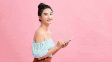 Yepyeni akıllı telefonunu inceliyor. Güzel genç kadınlar ellerinde akıllı telefonlar ve pembe arka planda dururken gülümsüyorlar.