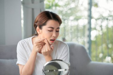 Genç bir kadın aynanın önünde sivilcelerini sıkıyor.