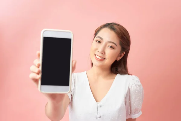 年轻女性展示的手机黑色屏幕 粉红背景下的微笑 把注意力放在手机上 — 图库照片