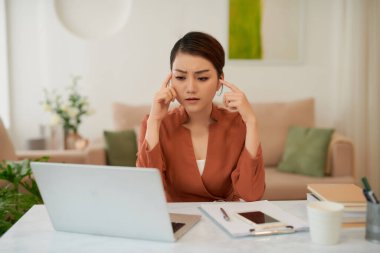 Güzel stresli genç bir ofis çalışanı ofiste acıdan başını tutup oturuyor.