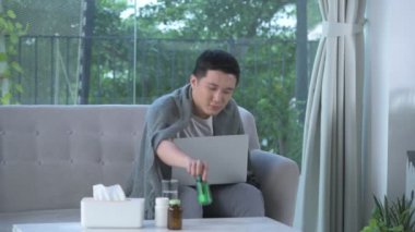 Kanepede dizüstü bilgisayarla acı çeken genç bir adam.