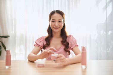 Sahne arkasında oturan zarif genç bir kadının profili kapalı gözlerle parfüm sıkıyor. Güzellik blogu için kamera kullanarak video kaydediyor.