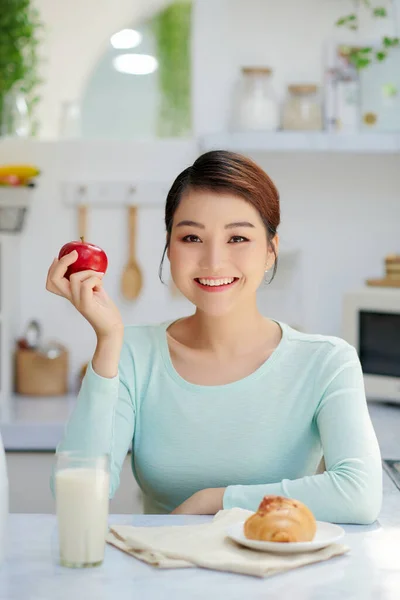 Girl sitting in kitchen on the desk with milk, apple and croissant