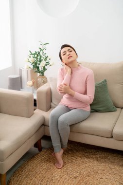 Evinde boynu ağrıyan genç bir kadın kanepede oturuyor.. 