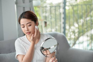 Neşeli, güzel Asyalı kadın taze cildine şeffaf pudra sürüyor.