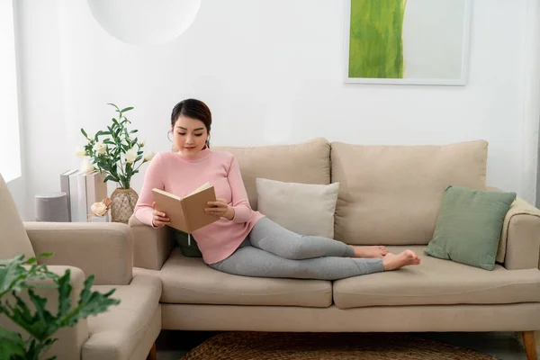 stock image Beautiful smiling woman reading a book and lying on the sofa in the living room