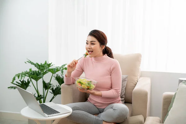 Bella Giovane Donna Seduta Sul Divano Mangiare Insalata Sana Usando — Foto Stock