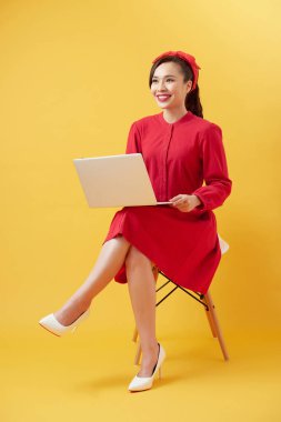 Sarı arka planda dizüstü bilgisayarla gülümseyen güzel kadın portresi.