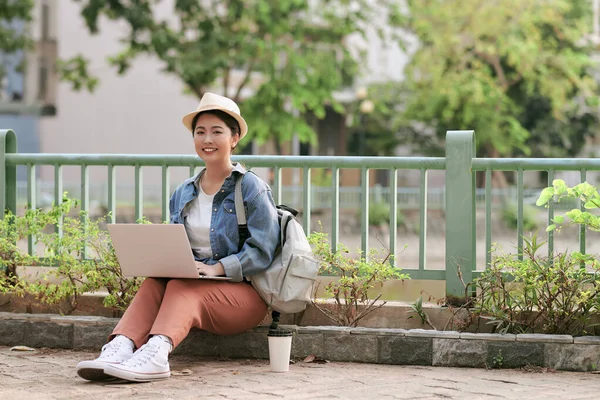 ノートパソコンで屋外に座っている間にノートパッドでノートを作る笑顔の若い女の子 — ストック写真