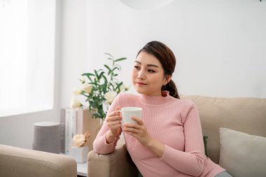 Evde bir fincan çayla mutlu genç bir kadın.