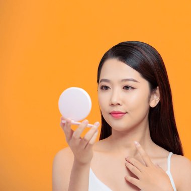 Gülümseyen kadın sarı arka planda ruj kullanıyor.