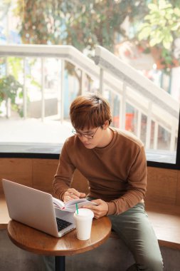 Genç adam kahve dükkanında okuyor ve okuyor.