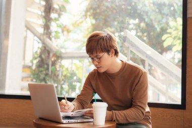 Odaklanmış bin yıllık öğrenci test için hazırlanan kafede kitaptan bilgi yazıyor.