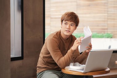 Asyalı genç bir adam kahvecide çalışıyor ya da okuyor.