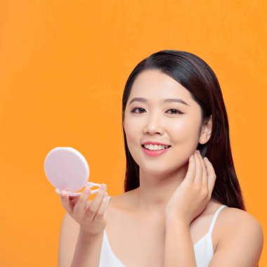 Güzel bir kadın sarı arka planda küçük bir aynaya bakıyor.