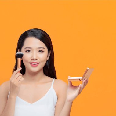 Asyalı genç güzel kadın gülümse ve eğlen, yüzüne dokun ve kozmetik tozu seti tut