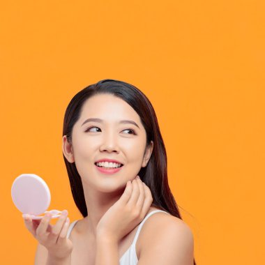 Çekici genç bir kadın küçük bir aynaya bakarken yüzüne dokunuyor.