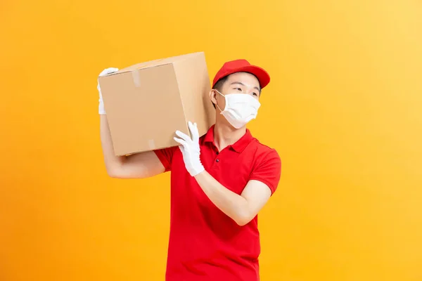 送货员穿着红帽空白T恤 制服面罩手套 拿着空纸板箱隔离在黄色背景下 — 图库照片