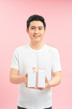 Gülümseyen yakışıklı adam pembe arka planda bir hediye kutusu sunuyor.