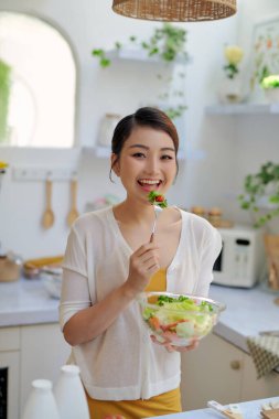 Genç ve güzel bir kadın evde taze salata yiyor.