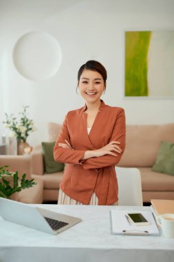 Siyah takım elbiseli ve çapraz kollu beyaz ofis odasında duran Asyalı çalışan kadın.,