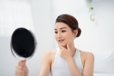 Asyalı genç kadın, günlük cilt bakımını yaptıktan sonra temiz ve sağlıklı yüz derisini hissediyor. 