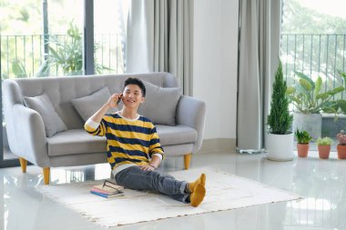 Kanepesinde beyaz bir arka planda oturan bir adam.