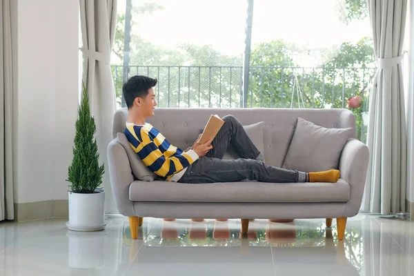 Portrait Joyful Young Man Reading Book While Sitting Sofa His — Stock Photo, Image