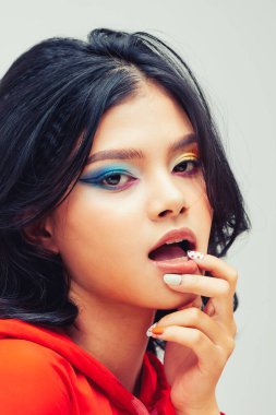 Stüdyo çekimlerinde genç ve güzel bir kadın ilginç bir yüz ifadesiyle yukarı bakıyor, ön parmağını dudağında tutuyor.