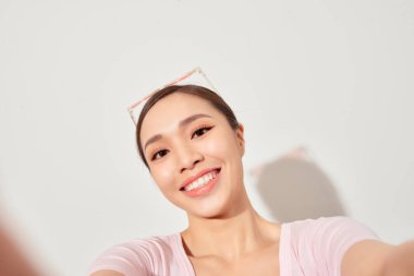 Gülen Asyalı genç kadın beyaz arka planda selfie çekiyor.