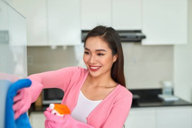 Genç Asyalı kadın mutfağı deterjan spreyiyle temizliyor..