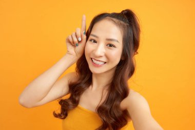 Sarı arka planda izole edilmiş akıllı telefondan selfie çeken gülümseyen güzel bir kadının portresi.