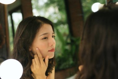 Aynadaki yansıma. Kadın aynaya bakar ve ilk kırışıklıkları fark eder.