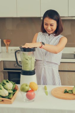 Güzel Asyalı kadın meyve suyu yapıyor. Mutfakta meyve suyu makinesiyle yeşil meyve suyu yapıyor. Sağlıklı konsept.