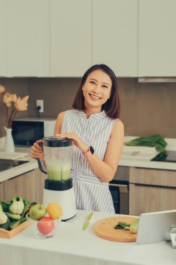 Sağlıklı Asyalı kadın evde blender ile yeşil sebze detoks arındırma ve yeşil meyve püresi yapmaktan hoşlanıyor. diyet konsepti. Sağlıklı yaşam tarzı.