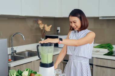 Genç Asyalı kadın mutfakta yeşil smoothie yapmak için blender kullanıyor..