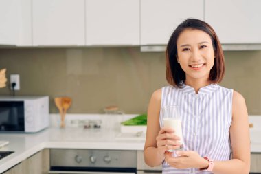 Güzel genç Asyalı kadın evdeki mutfakta süt içiyor..