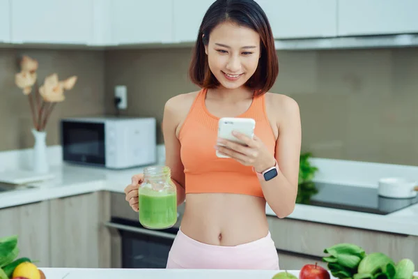 Жінка Використовує Телефон Обдумуючи Зелену Усмішку Стоячи Кухні — стокове фото