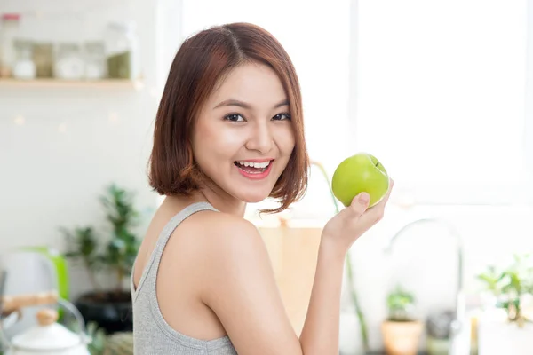 Happy Young Asian Woman Eating Green Apple on Kitchen. Diet. Dieting concept. Healthy food