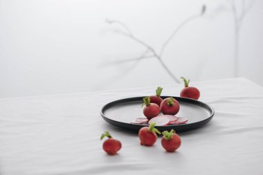 Kökleri ve sapı siyah bir tabakta taze kırmızı turplar.