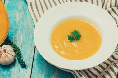 krem ve mavi ahşap zemin üzerine maydanoz ile kabak ve havuç çorbası.