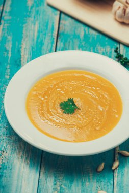 krem ve mavi ahşap zemin üzerine maydanoz ile kabak ve havuç çorbası.