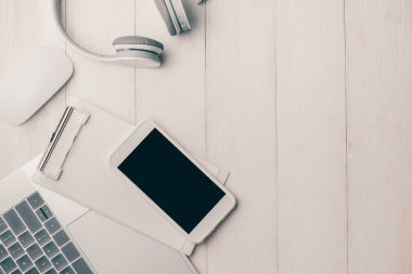Kulaklık ve akıllı telefonlu beyaz masadaki dizüstü bilgisayar. Yukarıdan görüntüle