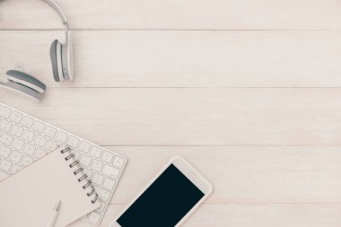 Not defteri ve bilgisayar klavyesi kulaklıklı beyaz masada. Yukarıdan görüntüle
